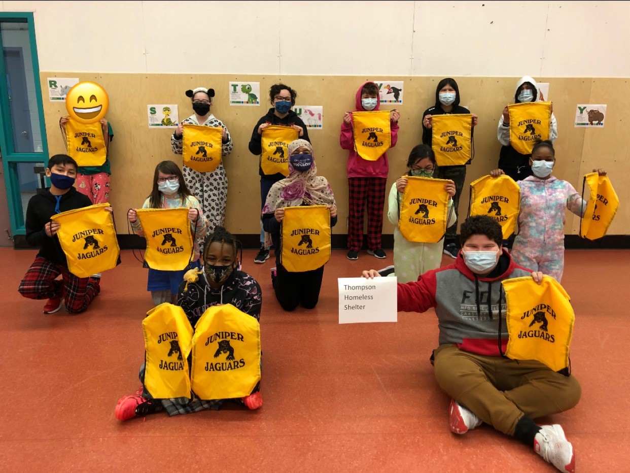 A group of elementary school students hold bright yellow cloth shopping bags full of goods for people seeking support at emergency shelters